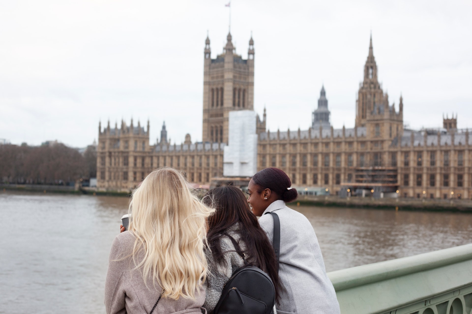 Három fiatal nő a Temze partján Londonban, mögöttük a Westminsteri palota